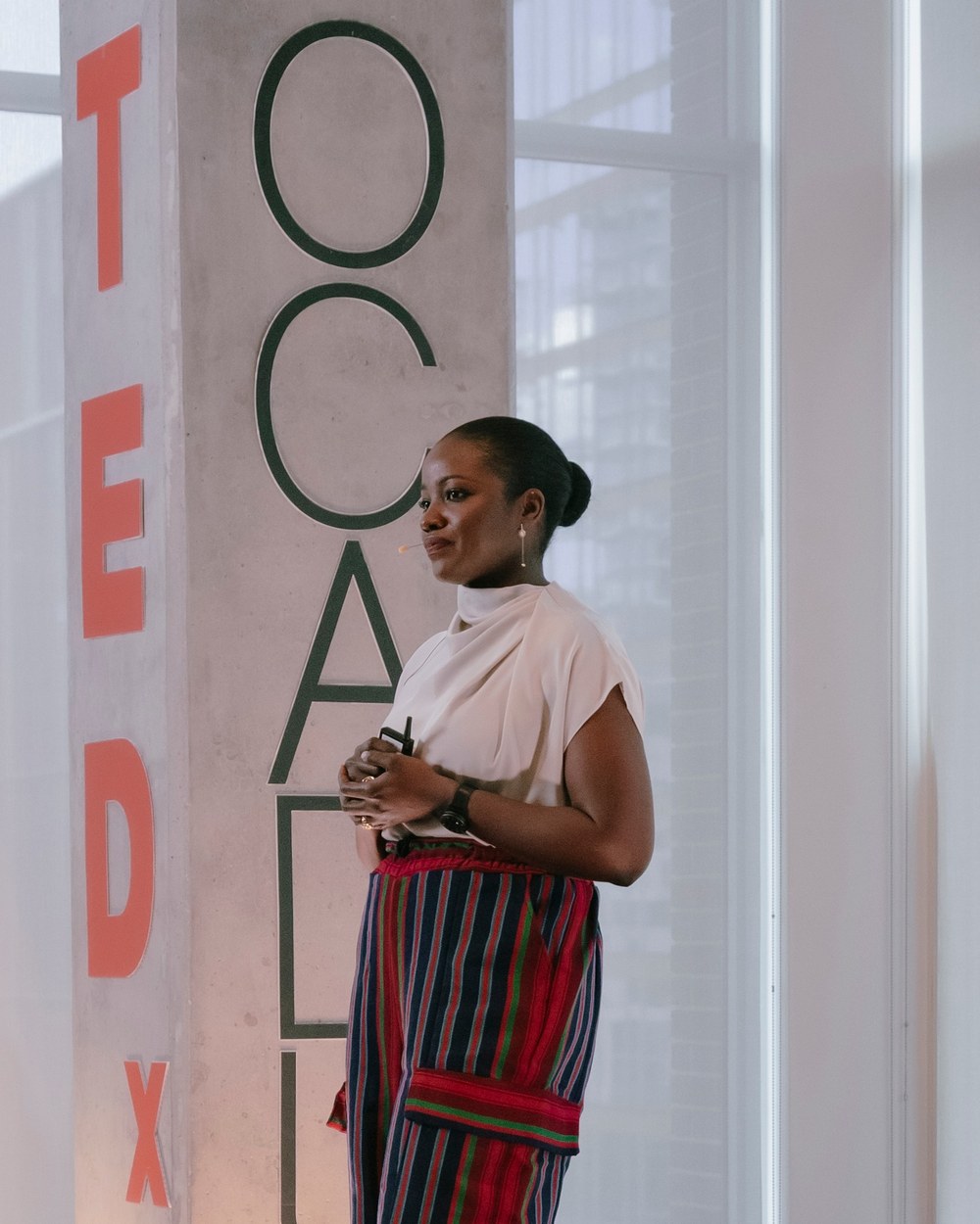 Dania Idam on stage at TEDxOCADU, smiling as she looks out at the audience, with the TEDx and OCADU lettering behind her.